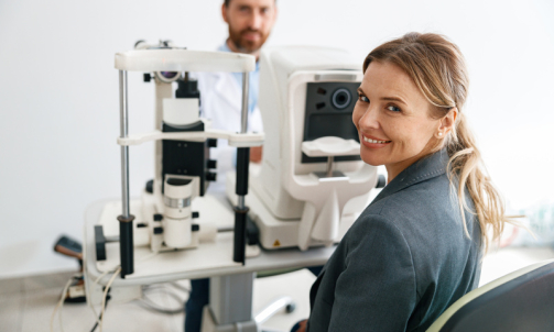 Smiling woman patient awaits vision test at opticians shop on the man optometrist background
