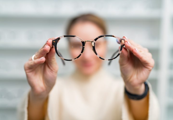 Woman is holding eyeglasses in her hands in optician store.